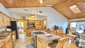 A spacious kitchen with wooden cabinets, a central island, and a dining area with wooden chairs. - Stunning Lakehouse with hot tub & tree house (Richfield Township)