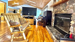 A cozy living room with a stone fireplace, wooden flooring, and a television in the background. - Stunning Lakehouse with hot tub & tree house (Richfield Township)