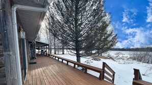 A wooden deck with a stone wall, a bench, and a view of a snowy landscape. - Stunning Lakehouse with hot tub & tree house (Richfield Township)