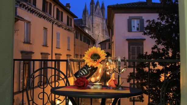 Un balcone con un tavolo apparecchiato per due, con bottiglia, bicchieri, una rosa e una candela.