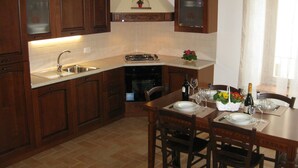 Una cucina con mobili in legno, un lavandino, un piano cottura e un tavolo da pranzo per due persone, completo di sedie.