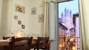 Un'area pranzo con tavolo apparecchiato per due, vista su un duomo attraverso una finestra e un balcone con ringhiera.