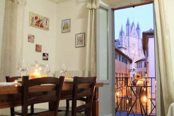 A dining area with a table set for two, a view of a cathedral through a window, and a balcony with a railing.