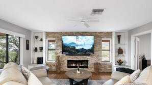 A modern living room with a stone fireplace, a flat-screen TV mounted above it, and a ceiling fan.