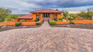 A house with a red-tiled roof, a stone facade, and a paved driveway leading to the entrance.