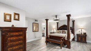 A bedroom with a four-poster bed, wooden dresser, and framed artwork on the wall.