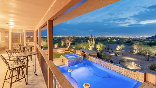 A balcony with a pool, outdoor furniture, and a view of a cityscape at dusk.