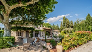 Une maison dotée d’un patio aménagé avec du mobilier d’extérieur, un grand arbre et un jardin bien entretenu.