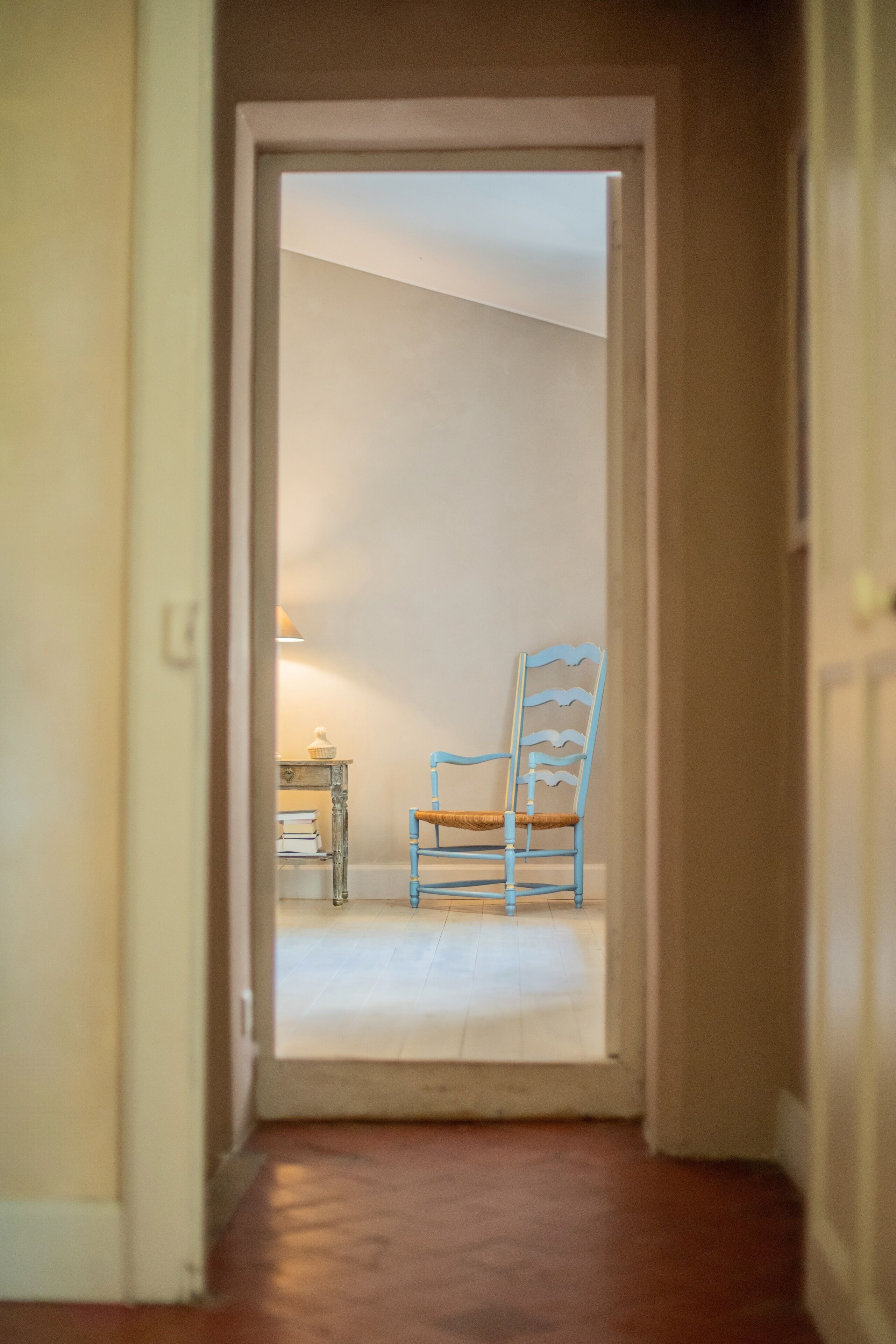 A narrow hallway leading to a room with a blue chair and a small table with books.