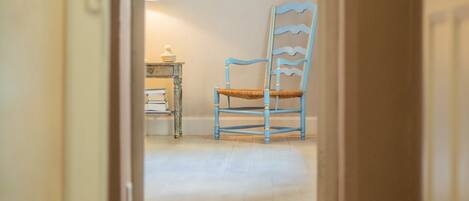 A narrow hallway leading to a room with a blue chair and a small table with books.