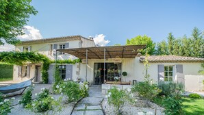 Une maison dotée d’un patio couvert, d’un jardin agrémenté de fleurs blanches et d’un chemin de gravier.