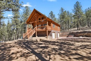 A wooden cabin with a porch, stone foundation, and a clear view of the surrounding forest. - Cozy Wooded Log Cabin | Hot Tub | Wood Stove | Games (Florissant)