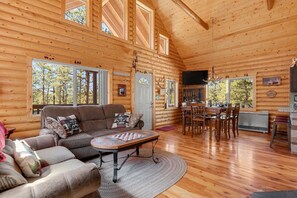 A log cabin interior with a living room, dining area, and kitchen. - Cozy Wooded Log Cabin | Hot Tub | Wood Stove | Games (Florissant)