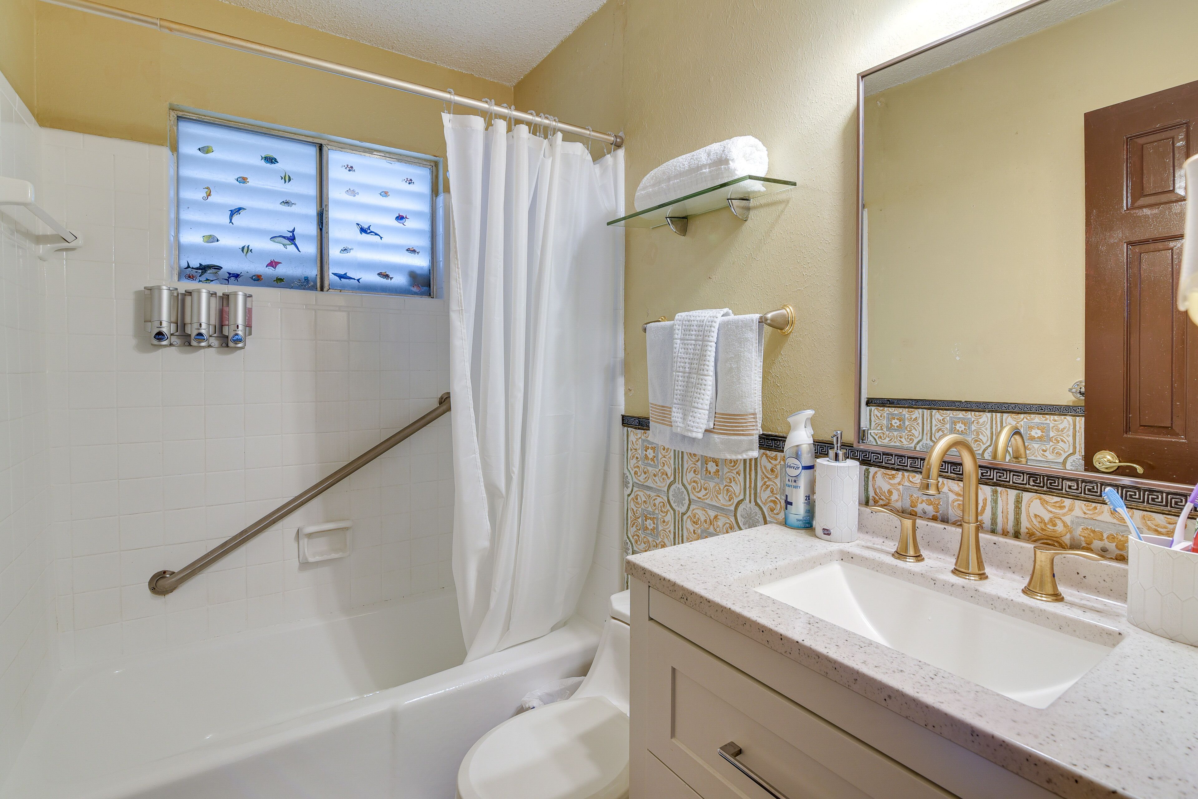 A bathroom with a bathtub, toilet, sink, and a shower curtain with a fish decal.
