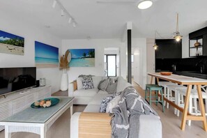 Un salon moderne avec un canapé, une table basse et un téléviseur. Il y a également un coin cuisine avec une table à manger et des chaises.