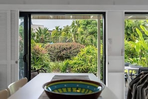A modern interior with a dining area, a view of a lush garden through glass doors, and a patterned bowl on the table.