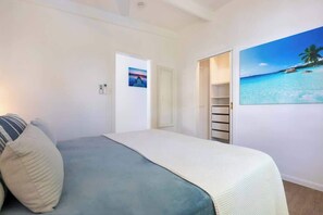 Una camera da letto con un letto, una porta che dà su un bagno e un quadro raffigurante una spiaggia.