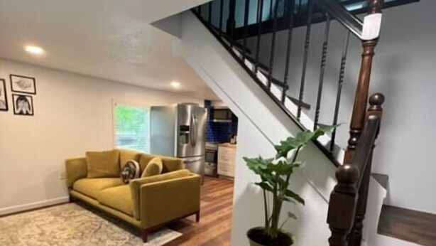 A modern living room with a wooden floor, a yellow sofa, a green plant, and a staircase with a wooden railing. - Tree Top Oasis Near Waco (Mart)