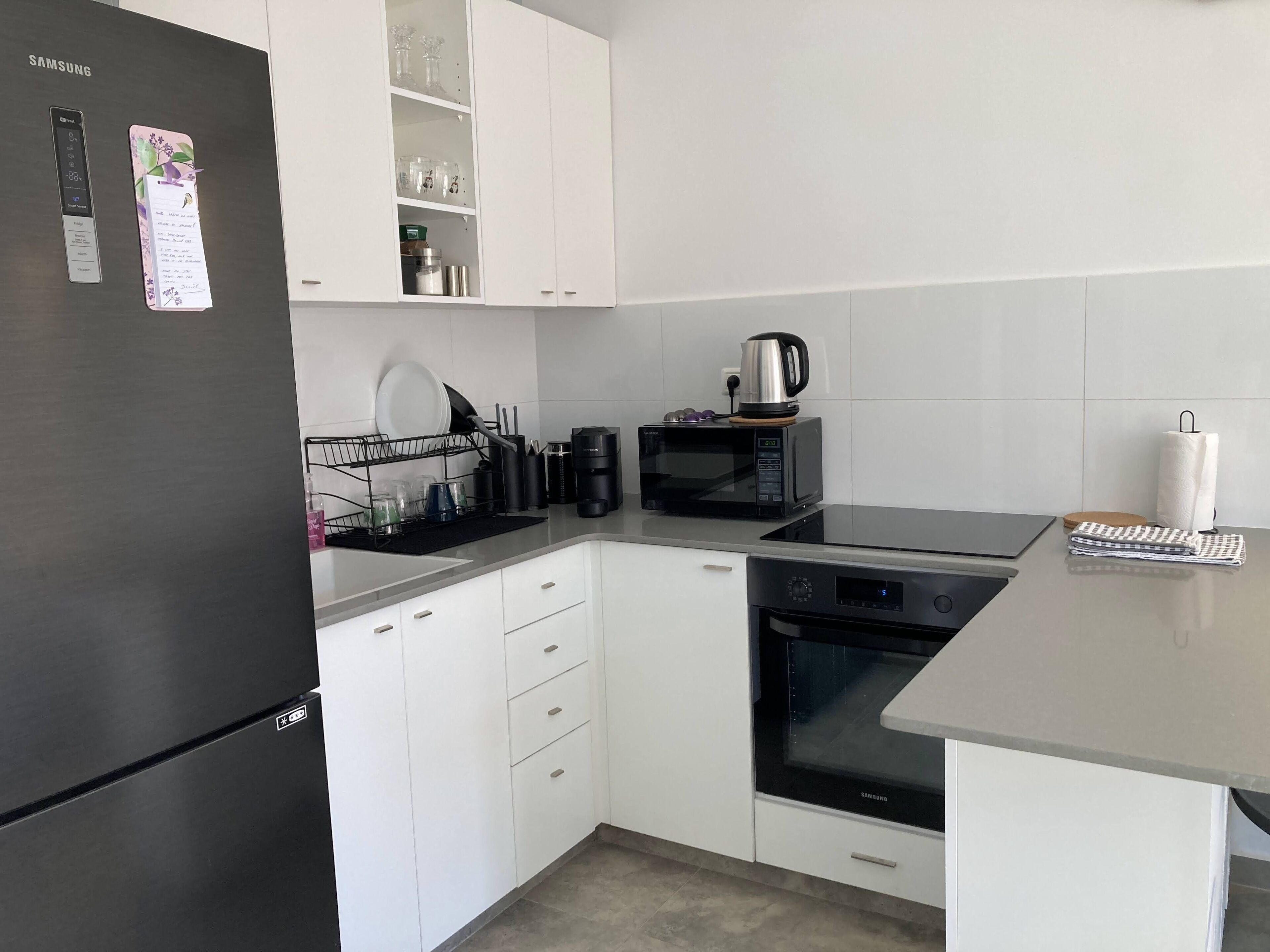 Eine moderne Küche mit weißen Schränken, einem schwarzen Kühlschrank, einer Mikrowelle, einer Kaffeemaschine und einem Samsung-Ofen.
