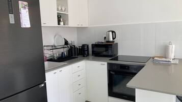 Eine moderne Küche mit weißen Schränken, einem schwarzen Kühlschrank, einer Mikrowelle, einer Kaffeemaschine und einem Samsung-Ofen.