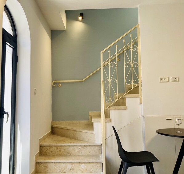 A staircase with a metal railing leading to a landing. A table with a chair is positioned on the landing.