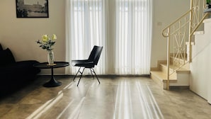 Een woonkamer met een zwarte stoel, een bijzettafeltje met een bloevas en een trap met een leuning.