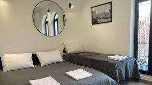 Een kamer met twee bedden, een ronde spiegel, een lijst met een afbeelding en een raam met uitzicht.