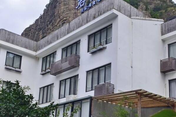 A hotel with a white facade, multiple balconies, and a mountain backdrop.