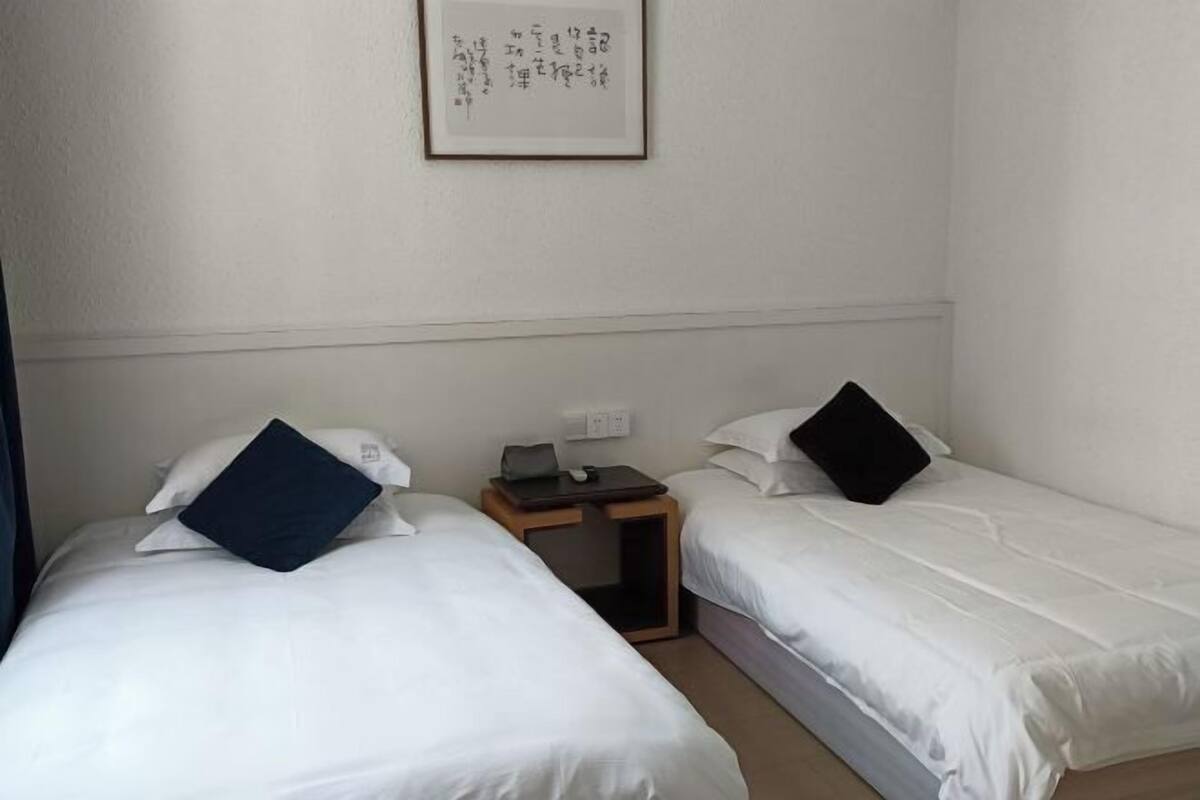 A hotel room with two beds, a small wooden nightstand, and a framed picture on the wall.