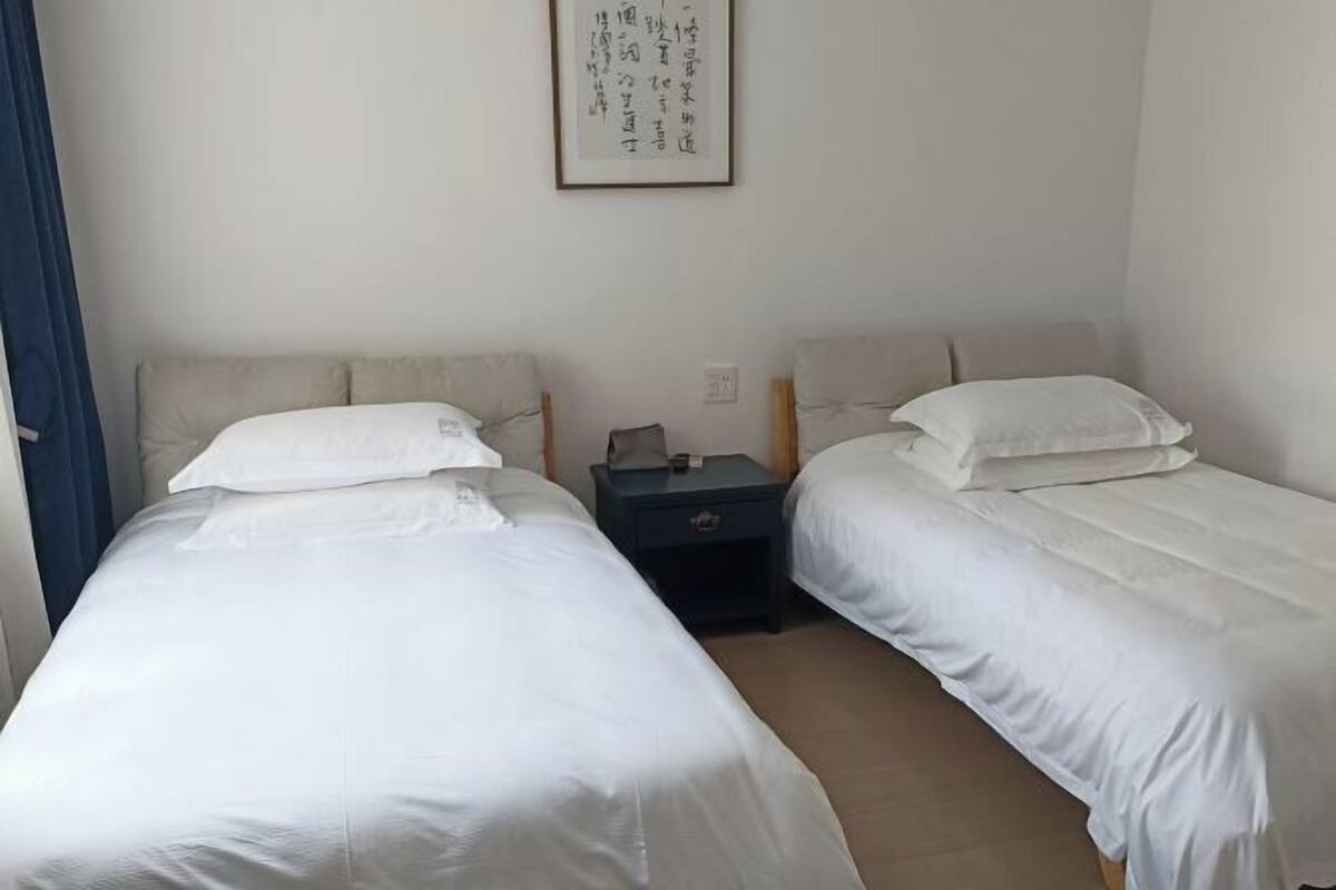 A room with two single beds, a small bedside table with a lamp, and a framed picture on the wall.