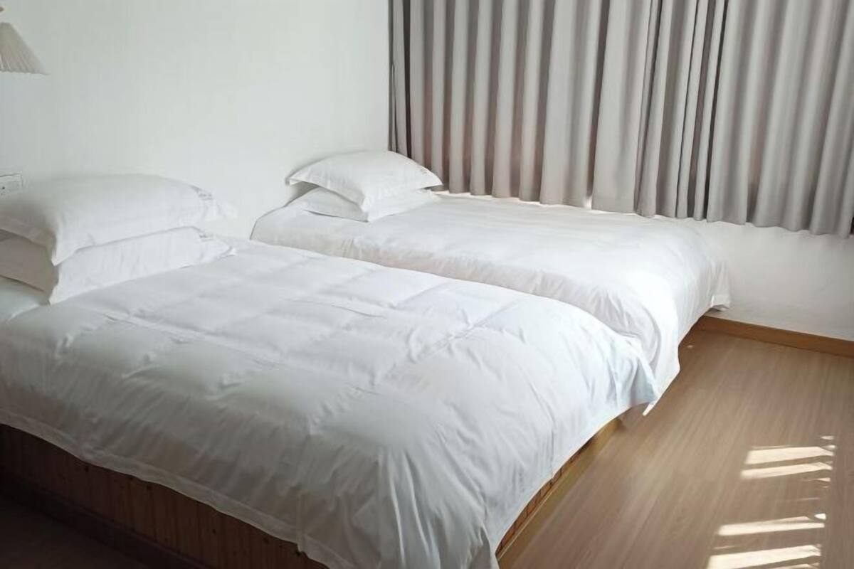 A hotel room with two beds, a wooden floor, and a window with curtains.