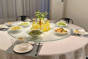 A round dining table with various dishes, drinks, and a small plant centerpiece.