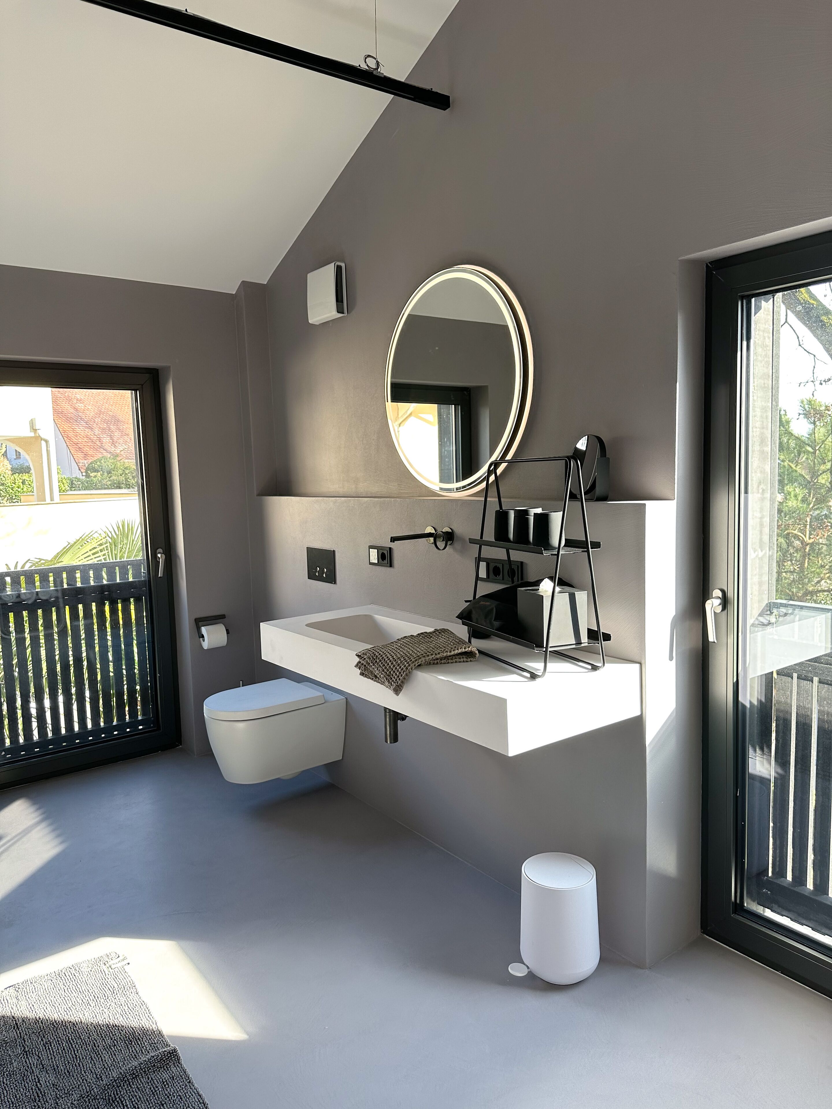 Une salle de bain moderne avec un lavabo blanc, un miroir rond avec éclairage intégré, une serviette et des toilettes.