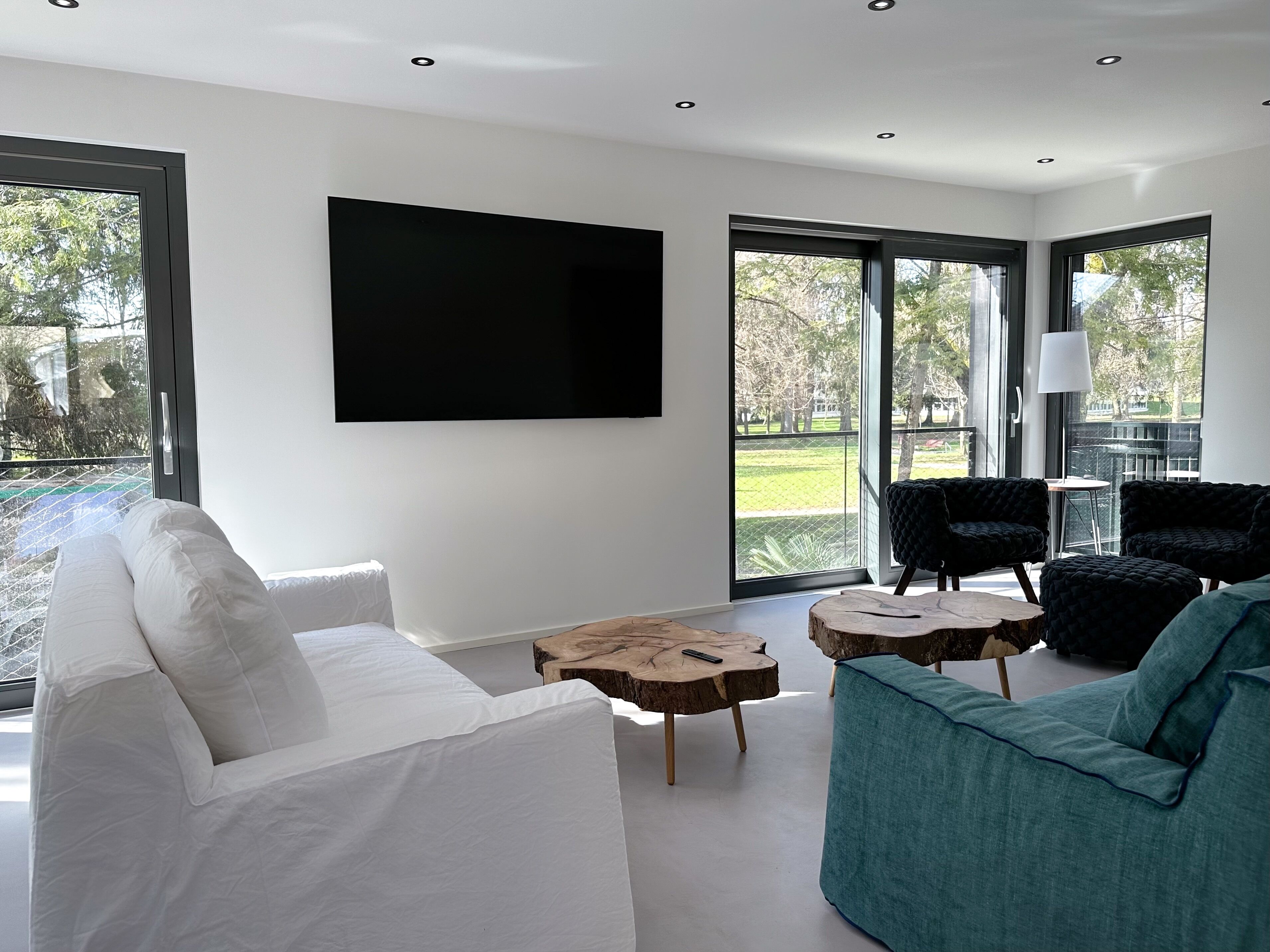 A modern living room with a white sofa, teal armchair, and a large flat-screen TV mounted on the wall.