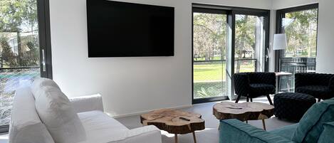 A modern living room with a white sofa, teal armchair, and a large flat-screen TV mounted on the wall.