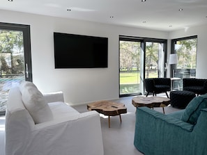 Un salon moderne avec un canapé blanc, un fauteuil turquoise et un grand téléviseur à écran plat fixé au mur.