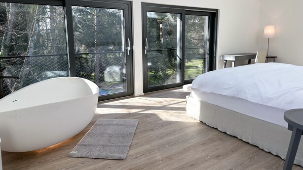 Un dormitorio con una cama grande, una silla moderna y vistas a un jardín a través de amplios ventanales correderas.