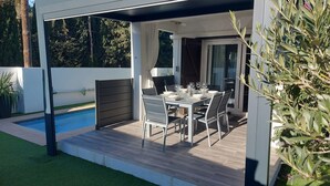A modern outdoor dining area with a pool, covered patio, and a view of the surrounding greenery. - Villa ideally located 10 minutes from the beach (L'Escala)