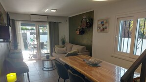 A modern living room with a wooden dining table, two chairs, a sofa, and a small round table with a lamp. - Villa ideally located 10 minutes from the beach (L'Escala)