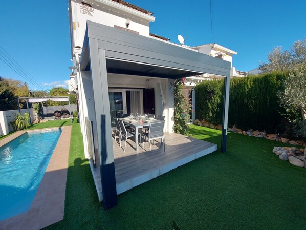 A modern house with a covered patio, a swimming pool, and a well-maintained garden.