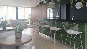 Ett modernt kök med en grön väggbeklädnad bakom arbetsbänken, vita stolar med metallben och en matplats med ett runt bord och krukväxter.