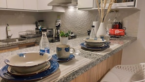 En köksbänk med olika rätter, en vattenflaska, en krukväxt och en röd väska.