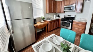 A compact kitchen with wooden cabinets, a stainless steel refrigerator, a microwave, and a stove. - Tower Grove Pet Friendly 2nd Floor Studio - 4 mi to SLU & Barnes -Shared Laundry (St. Louis)