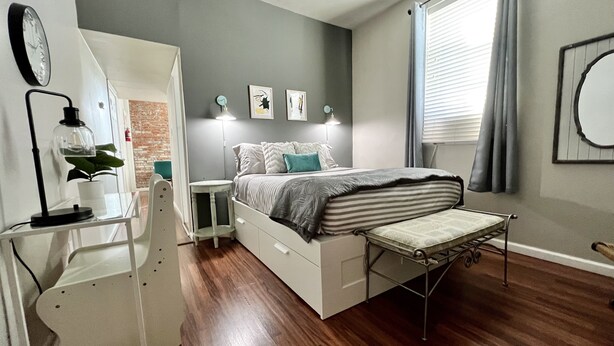 A bedroom with a bed, bedside tables, a desk, a chair, a plant, and artwork on the wall. - Tower Grove Pet Friendly 2nd Floor Studio - 4 mi to SLU & Barnes -Shared Laundry (St. Louis)