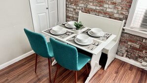 A dining area with a white table set for four, teal chairs, and a brick wall backdrop. - Tower Grove Pet Friendly 2nd Floor Studio - 4 mi to SLU & Barnes -Shared Laundry (St. Louis)