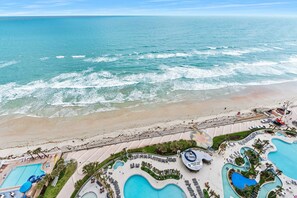 An aerial view of a beach resort with a large pool area, a beach, and the ocean.