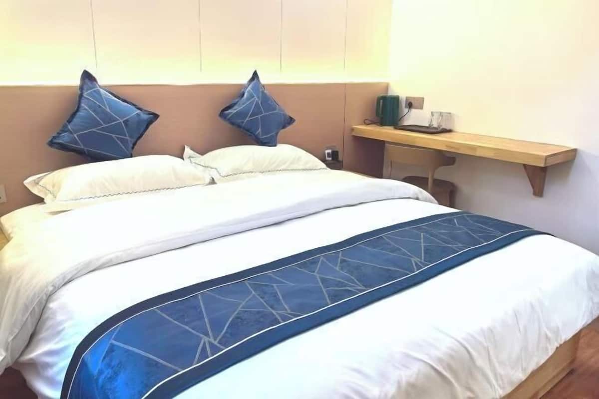 A bed with a white and blue bedspread, two pillows, a bedside table with a lamp, and a wall-mounted shelf.