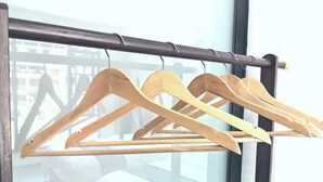 A wooden hanger rack with three hangers against a window with a view of buildings. - Lubianbian Inn (Zhangjiajie)