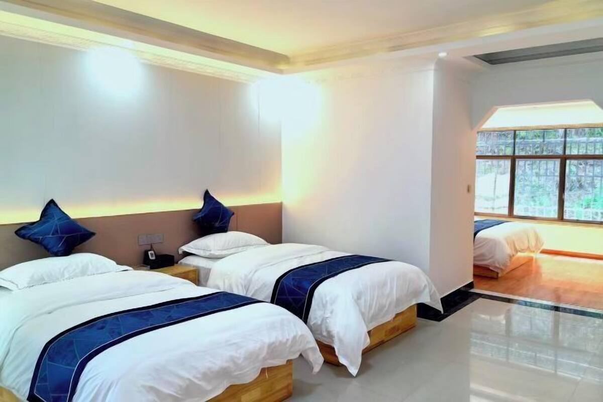 A hotel room with three beds, a large window, and a modern design.