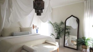 A bedroom with a large bed, a bedside table, a mirror, and a potted plant. - Mr. Nomad: Casa Bohem in Uptown (Dallas)